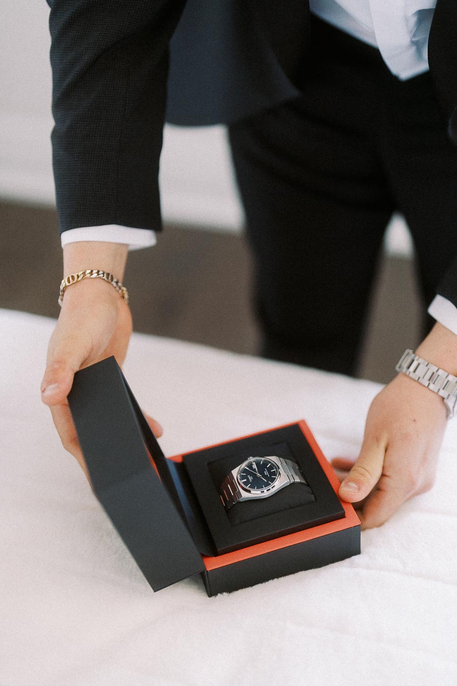 A person in a suit presenting a luxury wristwatch in an elegant black gift box, showcasing sophistication and style.