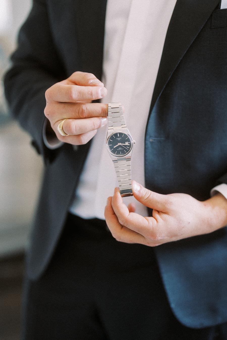 A man in a suit carefully holding a luxury silver wristwatch with a black dial, showcasing its elegant design.