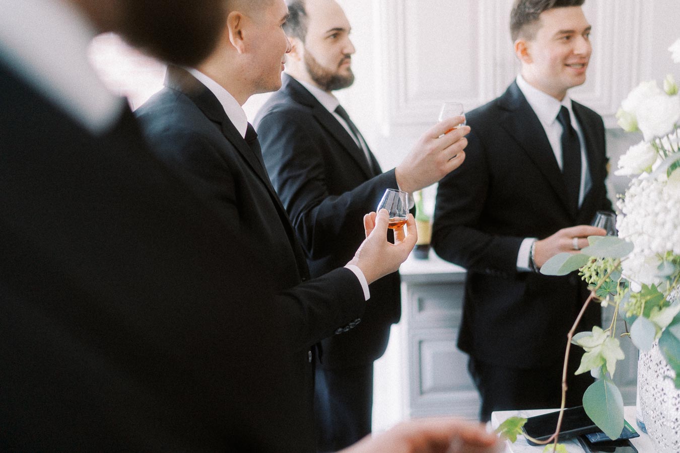 Men in suits holding glasses of whiskey at an indoor gathering.