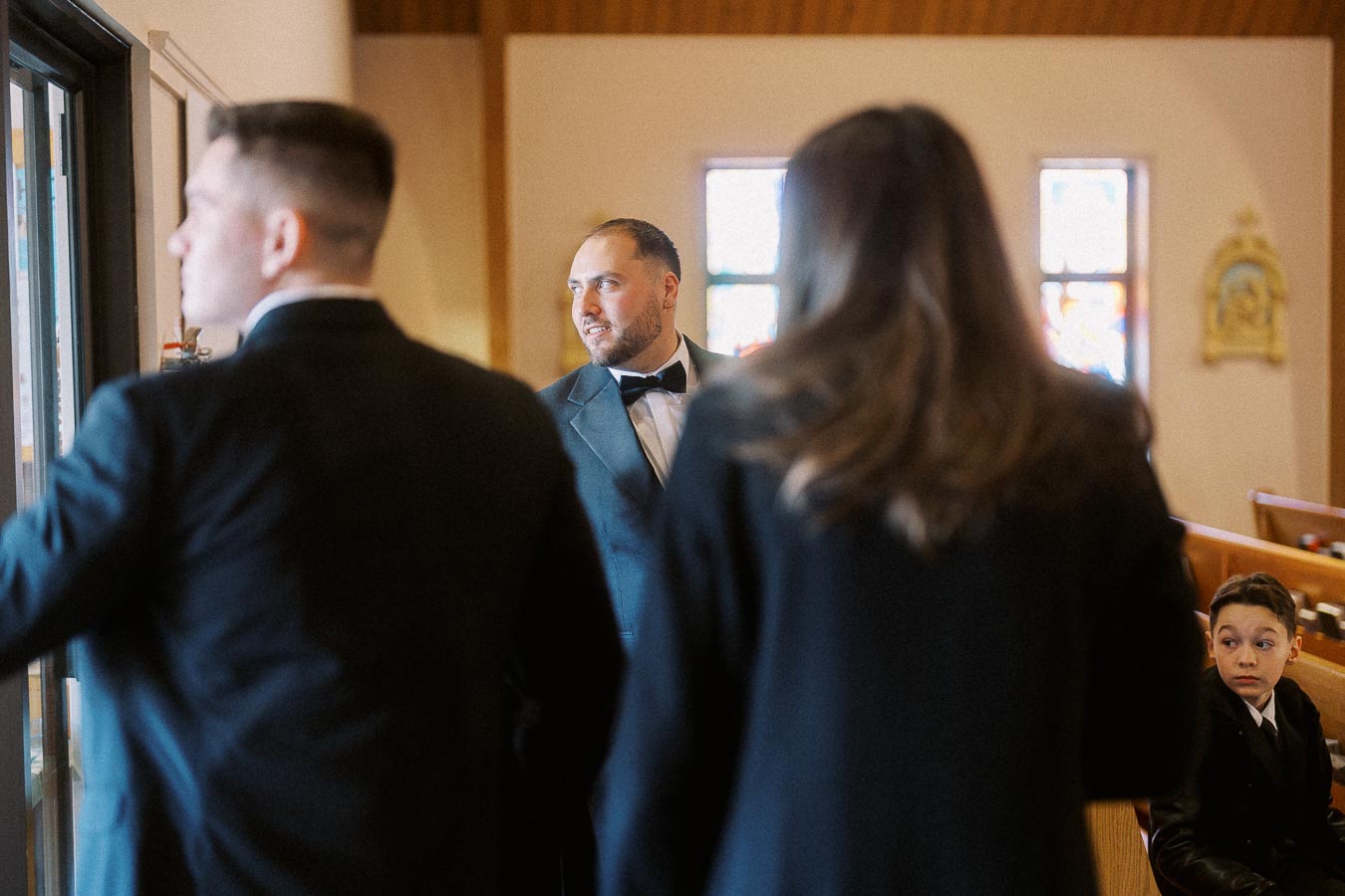 A group of people dressed in formal attire conversing inside a church, with stained glass windows in the background.