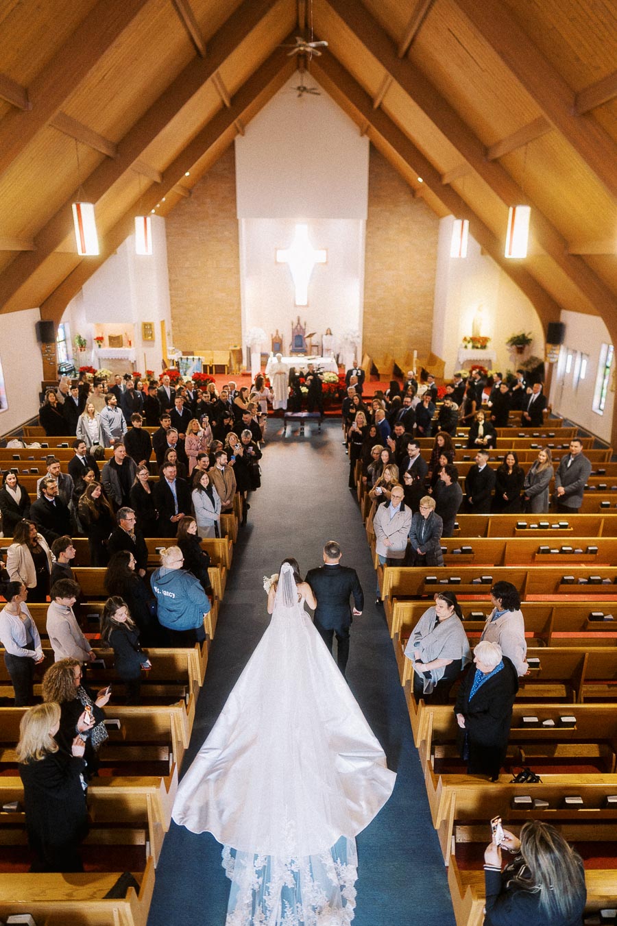 Bride walking down the aisle in a church, surrounded by guests, with a focus on the elegant wedding dress and the grand interior.