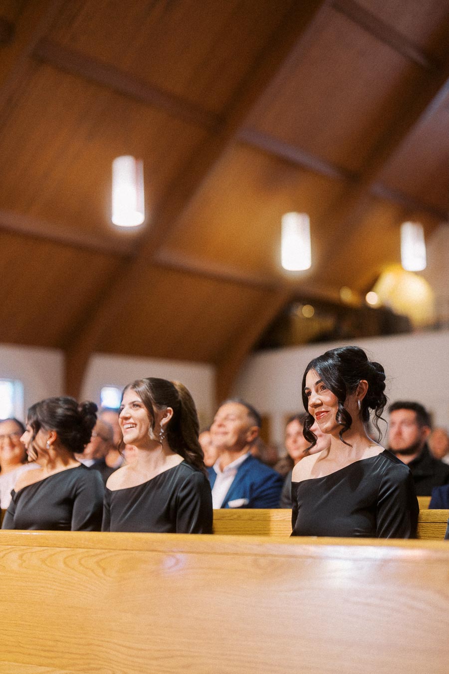 Women in matching black dresses seated in a church, smiling during a formal event.