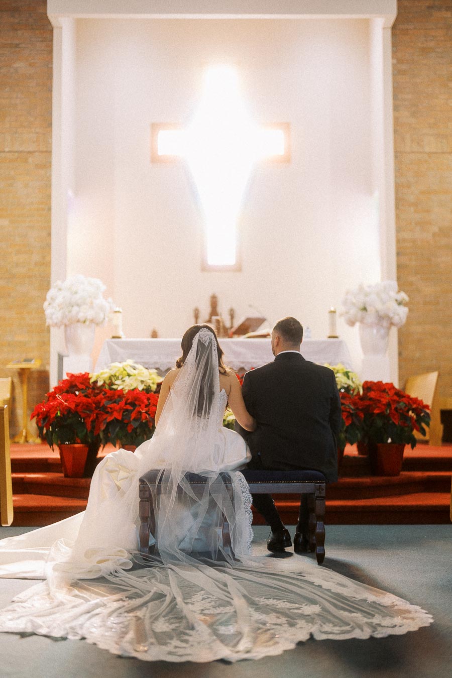Bride and groom kneeling before an altar adorned with flowers during a church wedding ceremony.