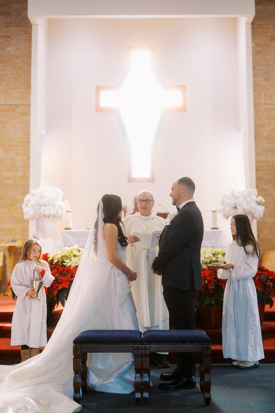 Bride and groom exchanging vows during a church wedding ceremony with altar server children assisting.