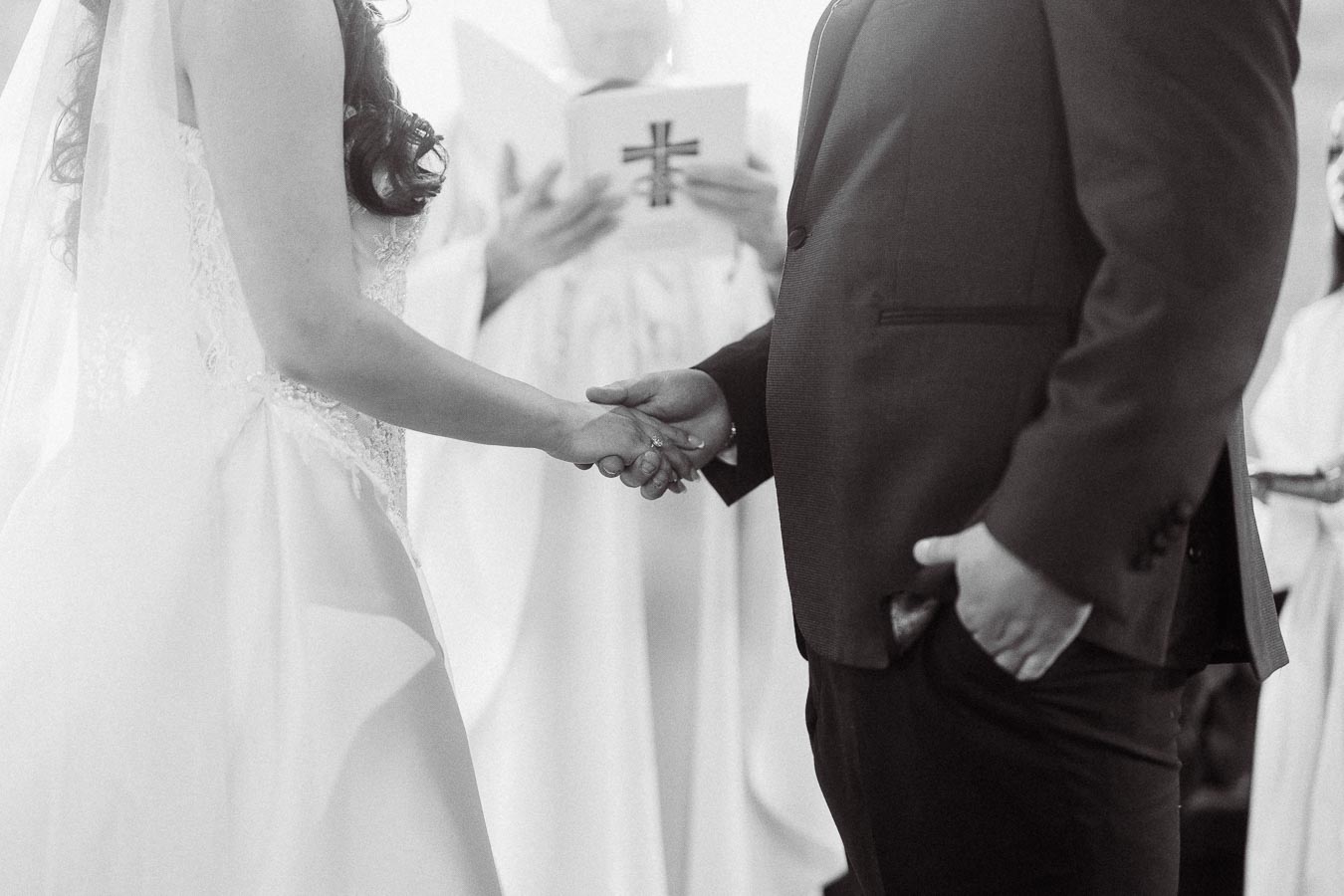 Wedding ceremony with couple holding hands, bride in a white gown and groom in a suit, exchanging vows in a church setting.