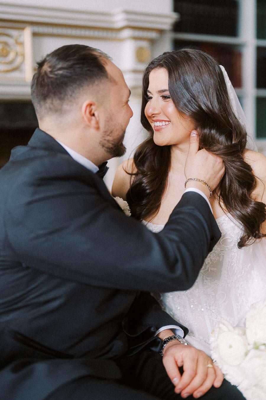 Smiling bride and groom in elegant attire sharing a tender moment indoors, traditional wedding setting.
