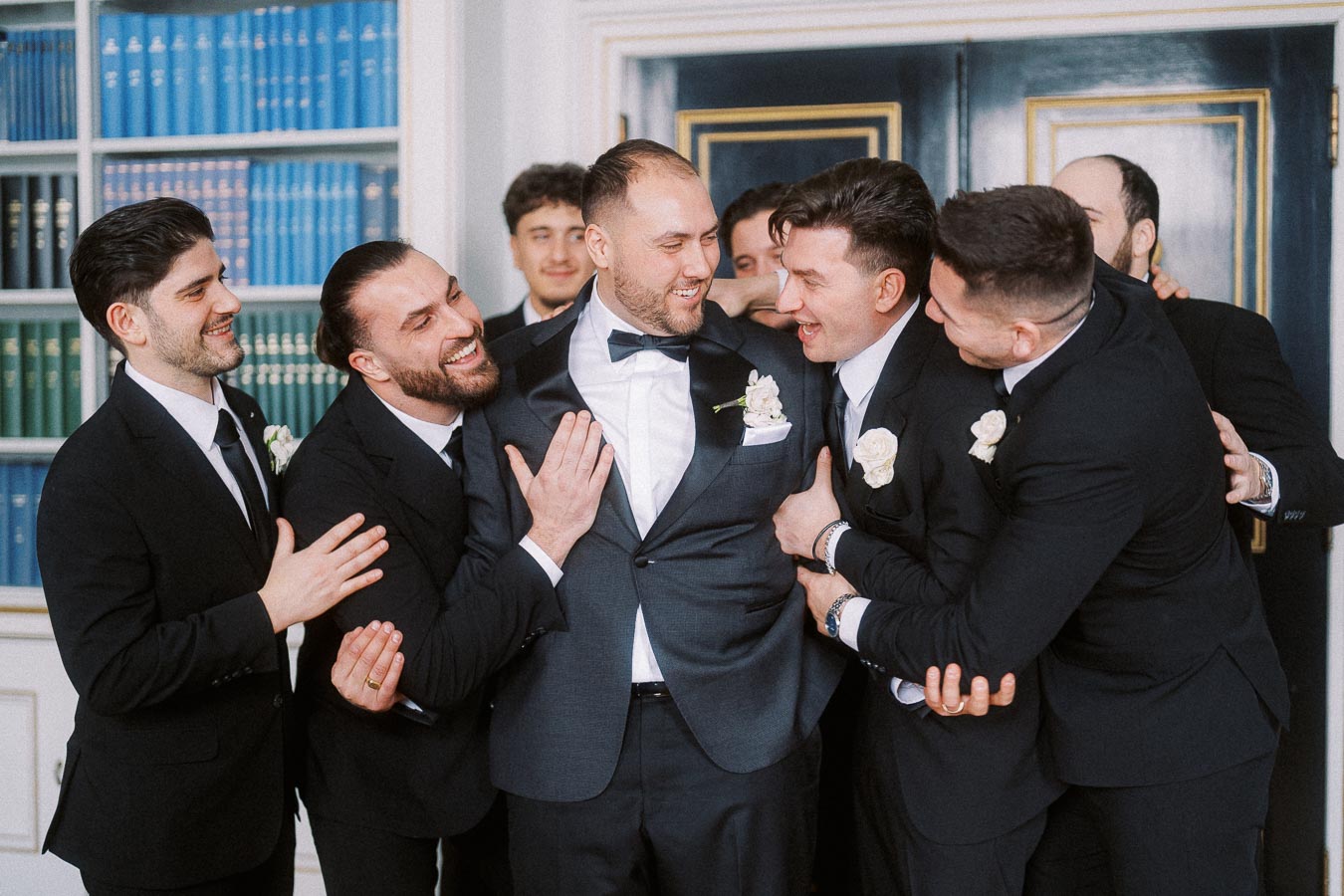 Groom and groomsmen laughing and embracing in formal attire, celebrating friendship and joy at a wedding event.