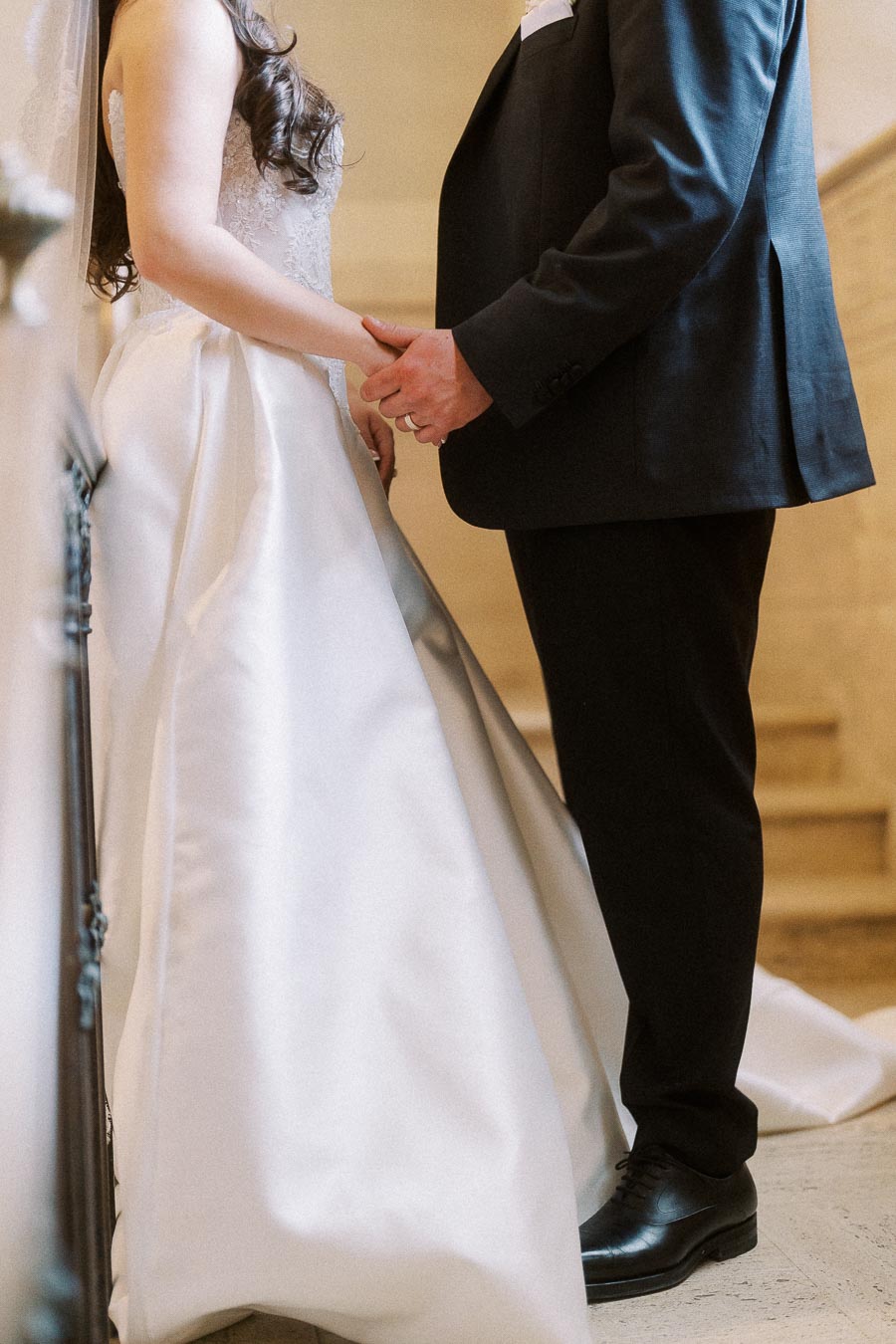 Bride and groom holding hands in elegant wedding attire, showcasing the bride's flowing gown and the groom's classic suit, symbolizing love and commitment on their special day.