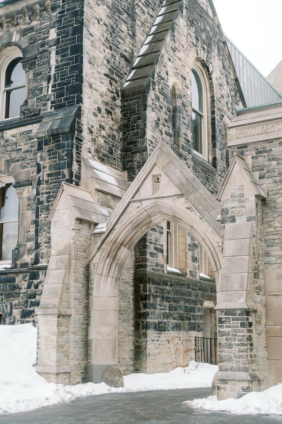 Historic stone building with gothic architecture featuring an arched entrance, covered in snow.