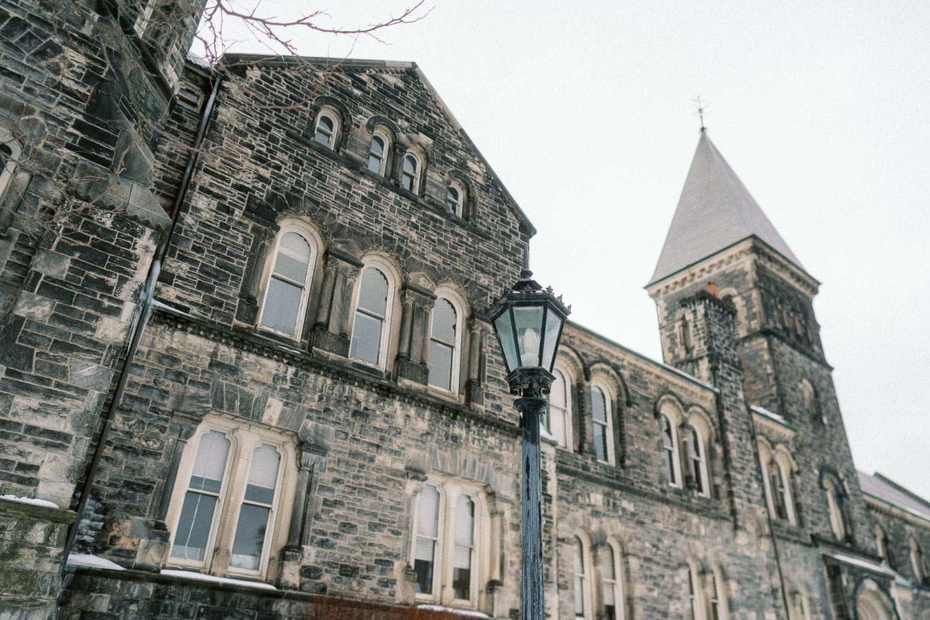 Historic stone building with arched windows and a vintage streetlamp in winter setting.