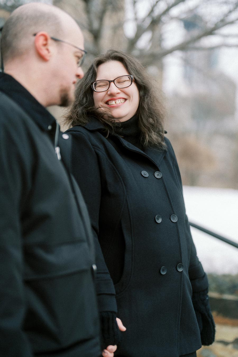 A happy couple enjoying a winter day outdoors, wearing warm coats and smiling at each other against a snowy backdrop.