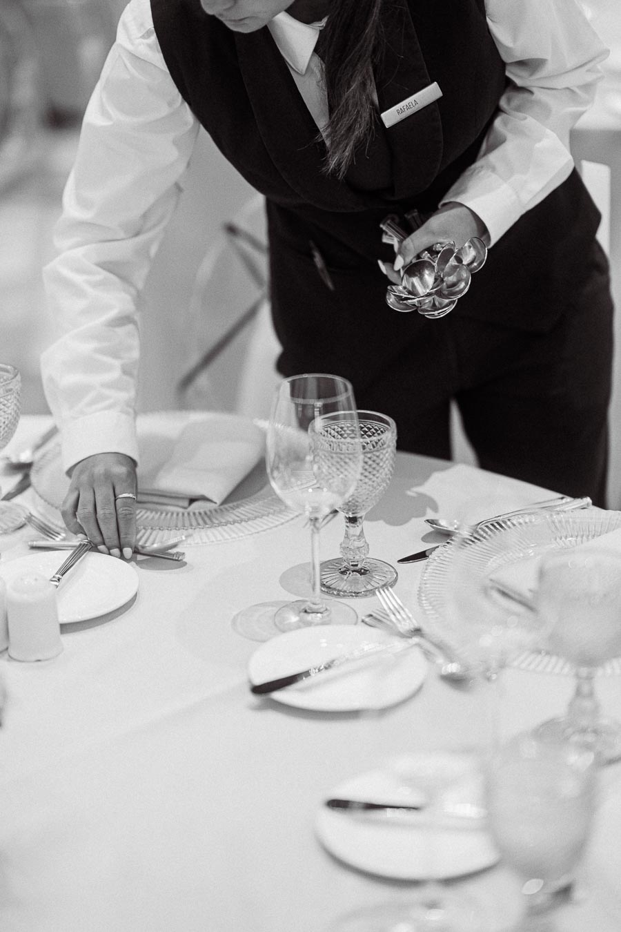 Server setting a formal dining table with elegant glassware and silverware in a restaurant.