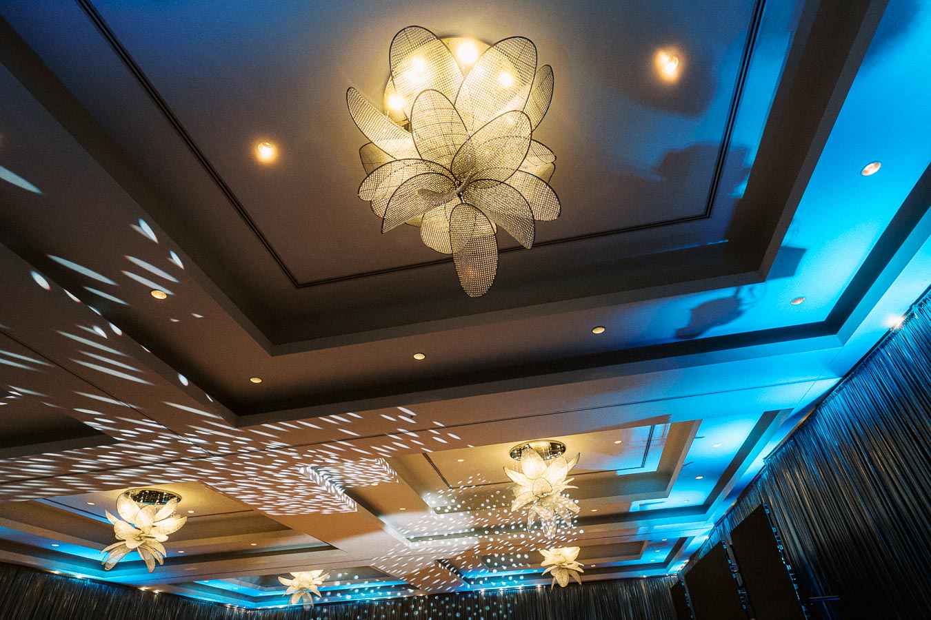 Elegant ceiling lights in a modern venue with blue ambient lighting and decorative shadows.