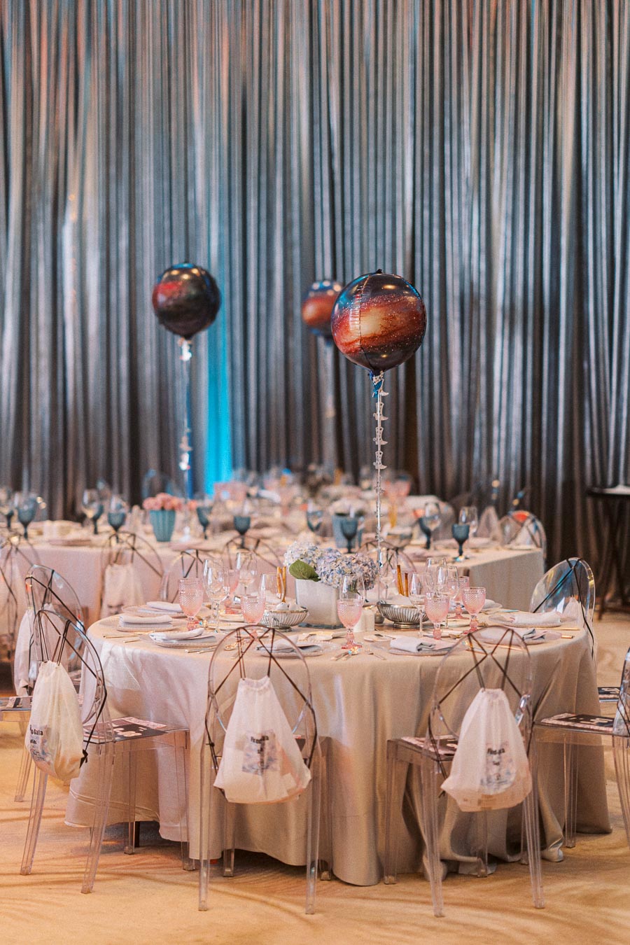 Elegant event space featuring beautifully set tables with crystal chairs and galaxy-themed balloons. The tables are adorned with fine dining settings, creating a sophisticated ambiance perfect for a stylish celebration or corporate event.