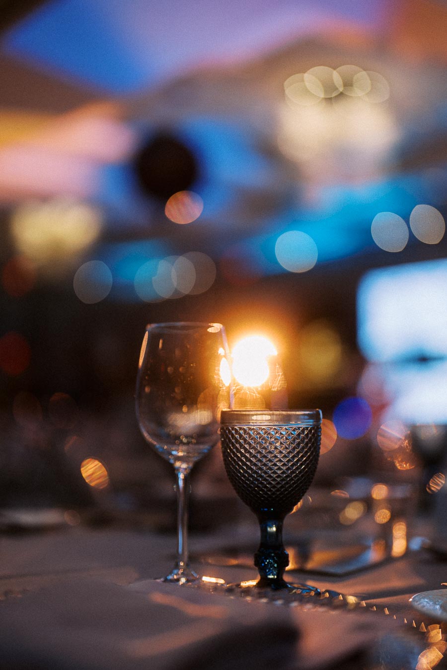 Elegant wine glasses on a softly lit table with a glowing candle, creating a warm and intimate dining atmosphere.