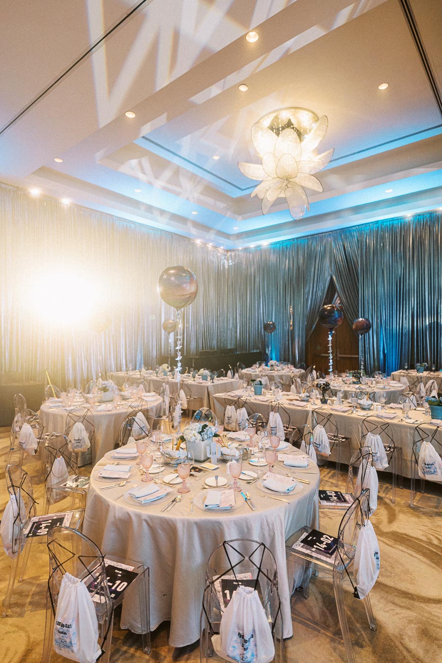 Luxurious event hall decorated for a corporate gala with elegantly set round tables, translucent chairs, and soft lighting.