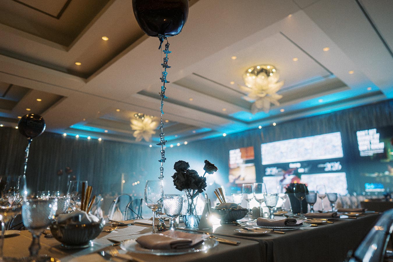 Elegant banquet hall with intricately set tables, featuring floral centerpieces, balloons, and ambient lighting, ready for a formal event or celebration.