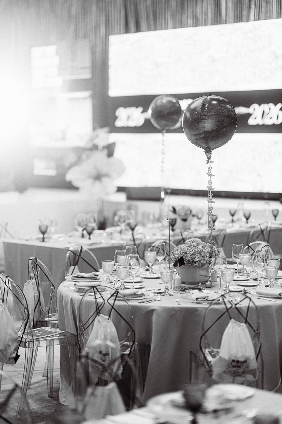 Elegant black and white banquet setting with round tables, transparent chairs, intricate tableware, and decorative balloons, showcasing a sophisticated event ambiance.