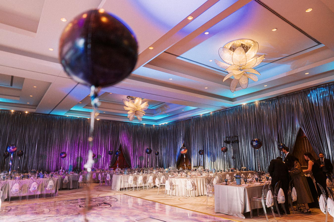 Luxurious ballroom decorated for a formal event with elegant lighting, chandeliers, and tables set with white linens.