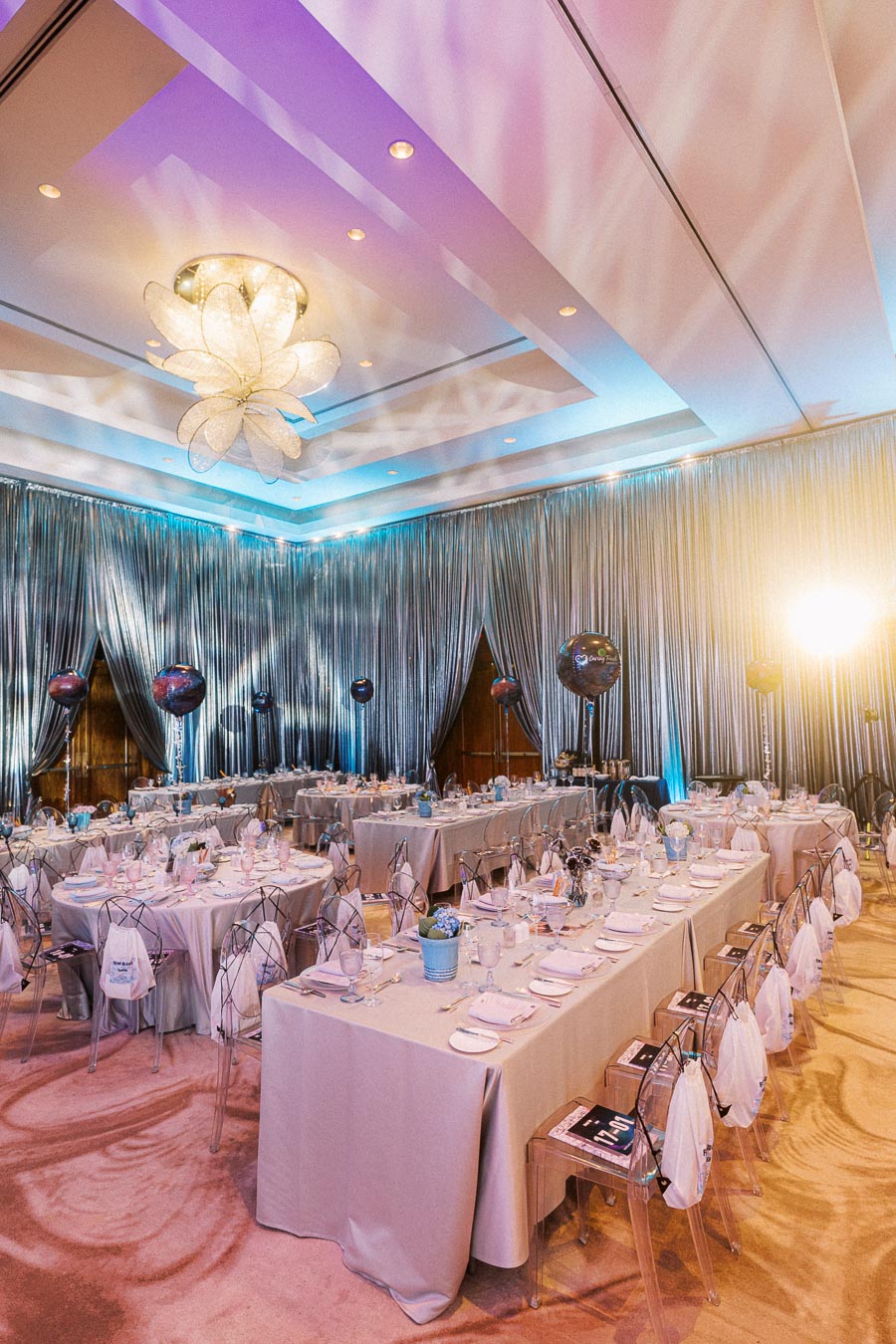 Elegant banquet hall setup with draped silver curtains, modern lighting, and neatly arranged tables ready for a formal event.