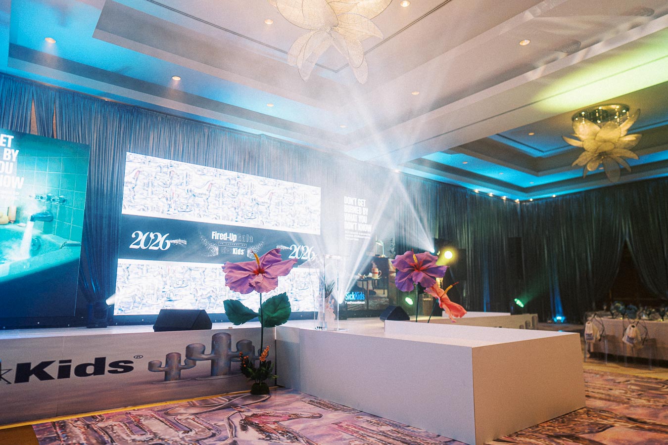 Stage setup at the 2026 Fired-Up Gala for SickKids, featuring vibrant lighting, large decorative flowers, and digital display panels in a lavishly decorated venue.