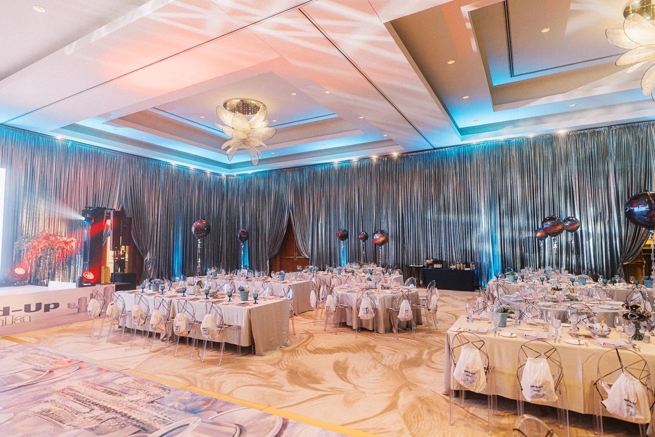 Elegant banquet hall set for a sophisticated event with round tables, clear chairs, and ambient lighting; chic decor creates an inviting atmosphere for a wedding reception or corporate gala.