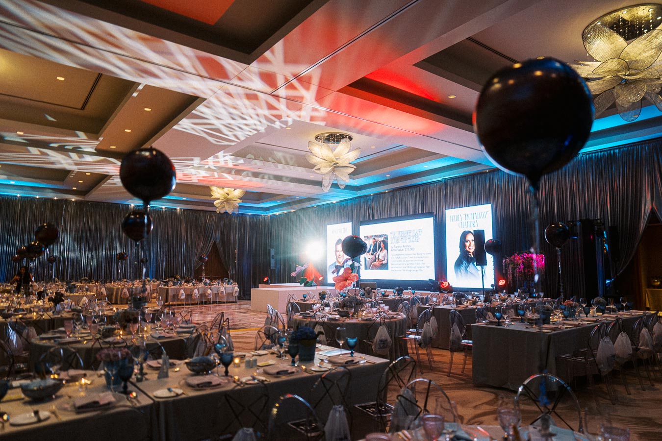 Elegant banquet hall setup with decorated tables, colorful lighting, and large display screens for a glamorous event or celebration.