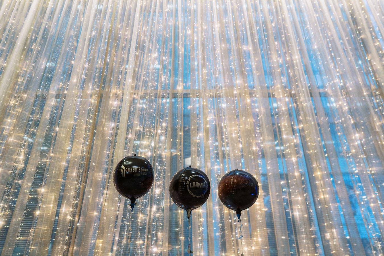 Luxurious event decoration with shimmering string lights and three black balloons, creating an elegant ambiance against a sparkling backdrop.