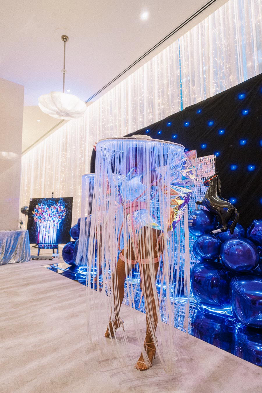 Futuristic costume with LED lights and fringe on display at a vibrant, modern art event with blue and iridescent decor.