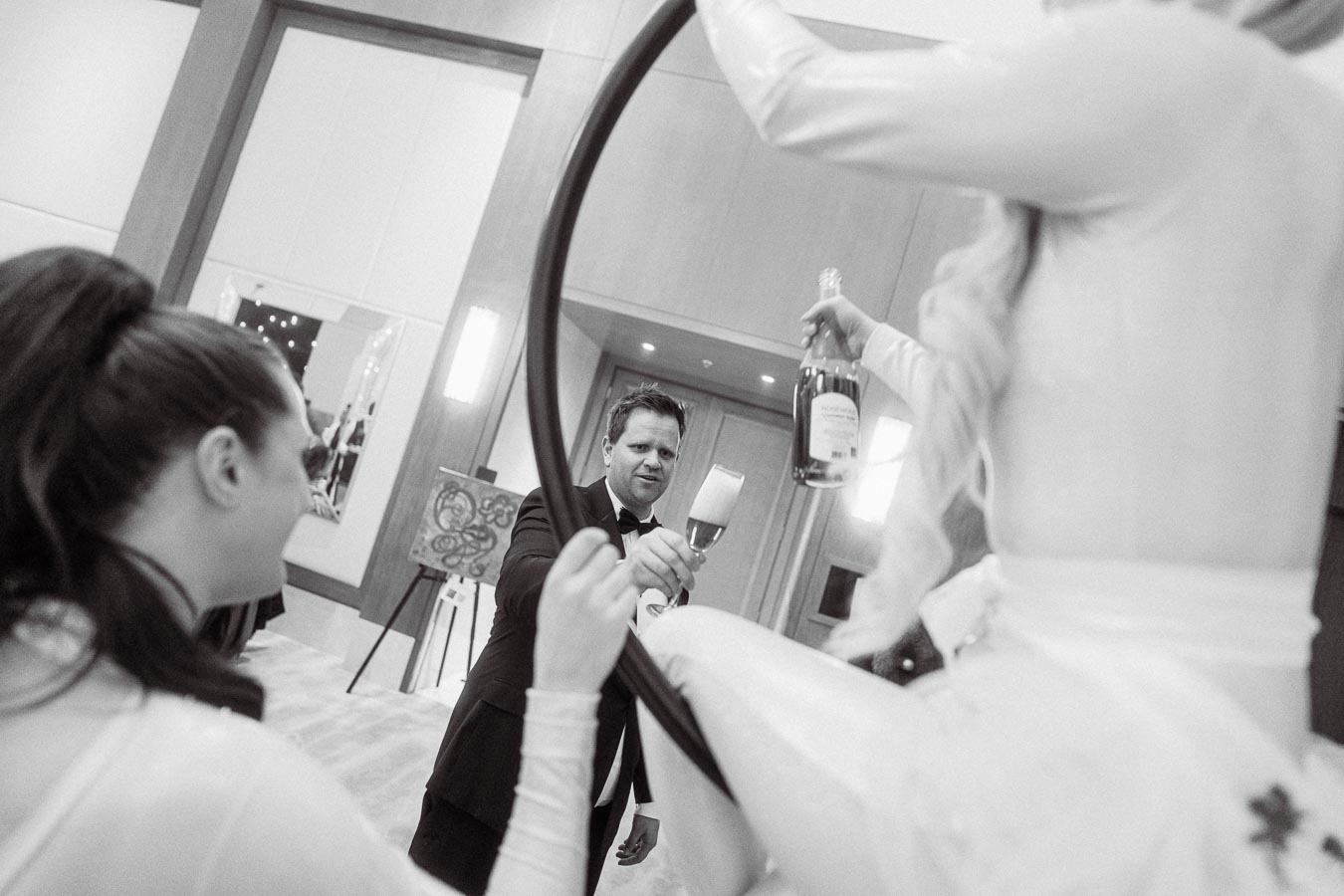A man in formal attire with a bowtie receiving a glass of champagne from a woman performing on a hoop at an elegant indoor event.