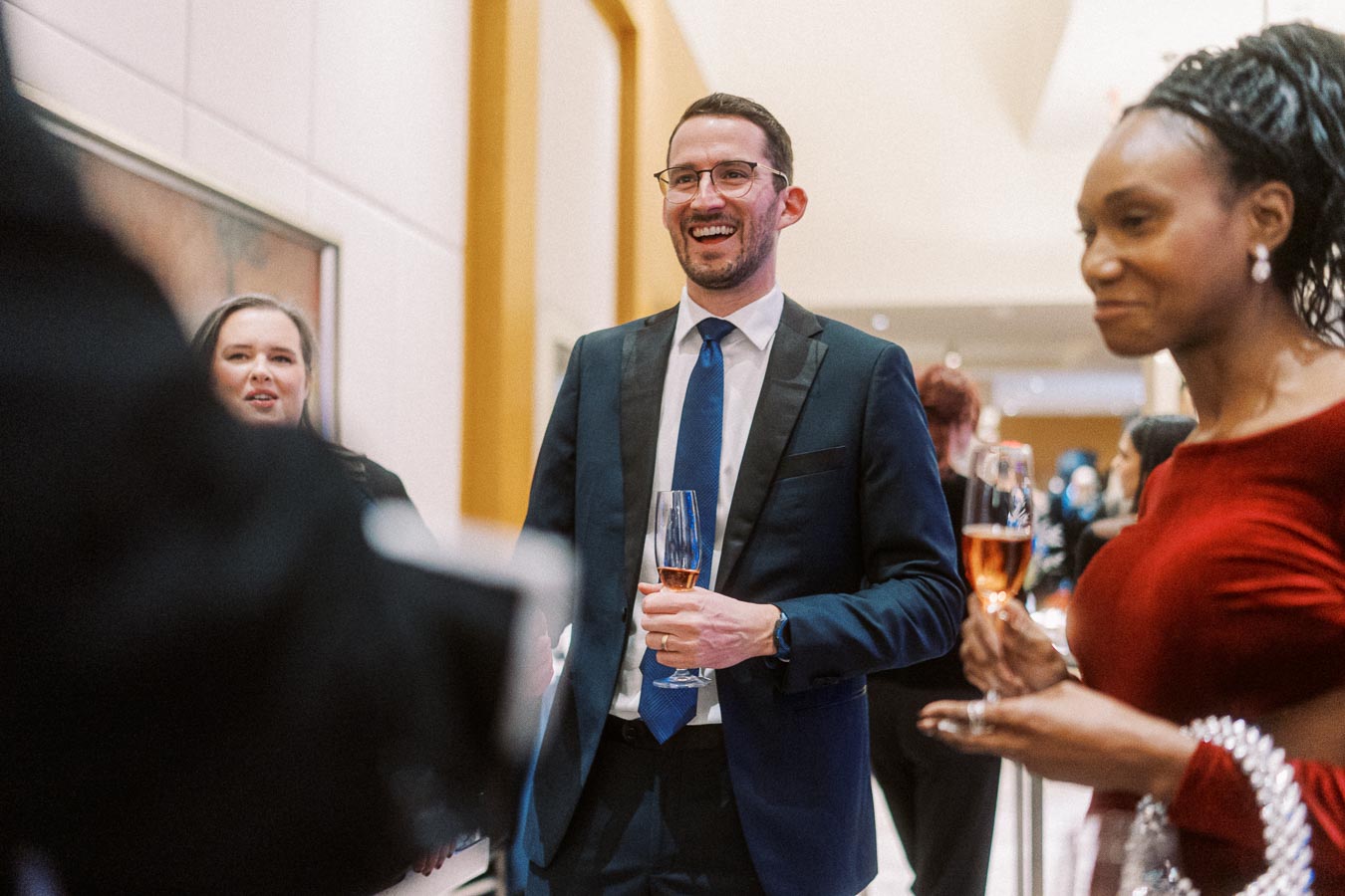A group of elegantly dressed people socializing at a formal event, holding champagne flutes and engaging in conversation.