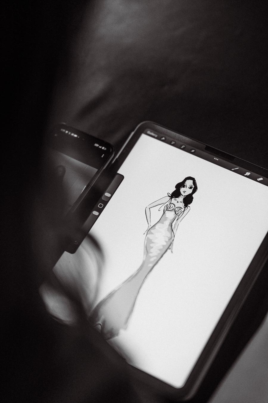 Black and white digital illustration of a fashion design sketch on a tablet, showcasing a stylish woman in an elegant gown.