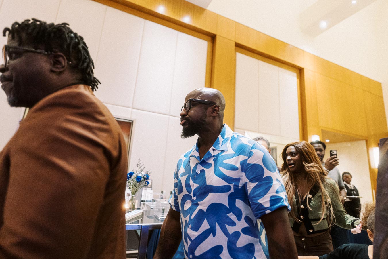 Group of people socializing at an indoor event, one wearing a distinctive blue and white patterned shirt.