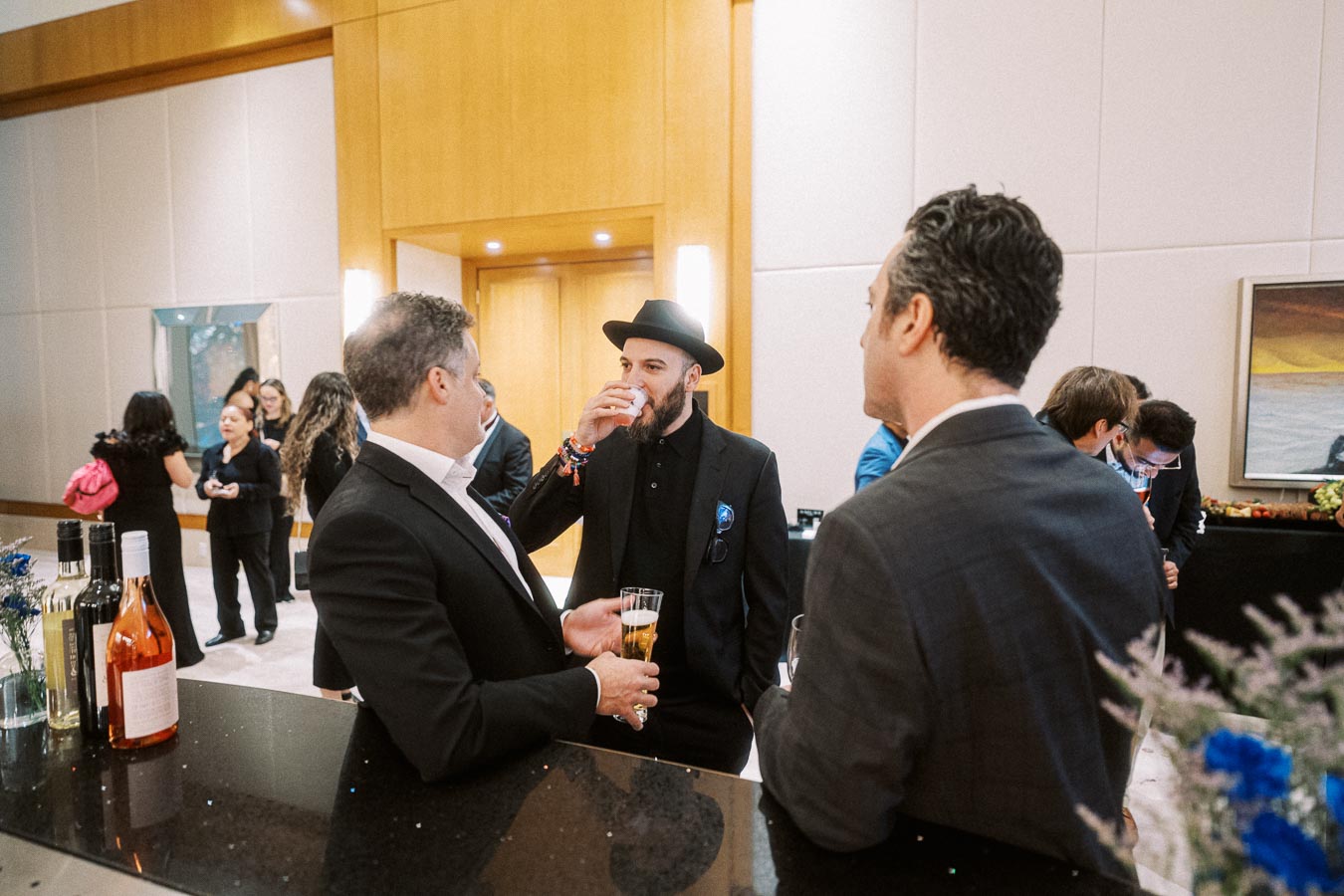 Group of professionals networking at a formal event, engaging in conversation at a bar with drinks, showcasing social interaction and business networking environment.