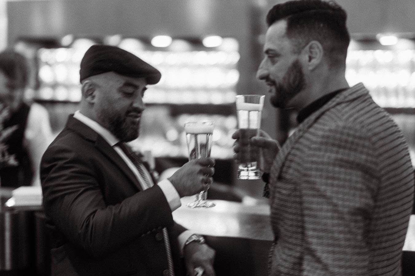 Two stylish men dressed in suits enjoying a conversation over beers at a sophisticated bar.