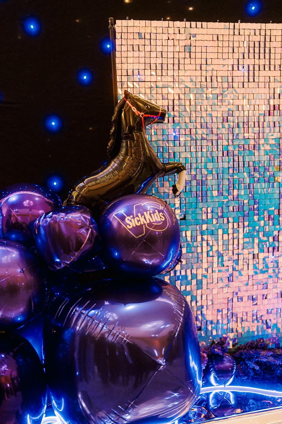 Decorative balloon display featuring a horse-shaped balloon surrounded by purple balloons with SickKids branding at an illuminated event backdrop.