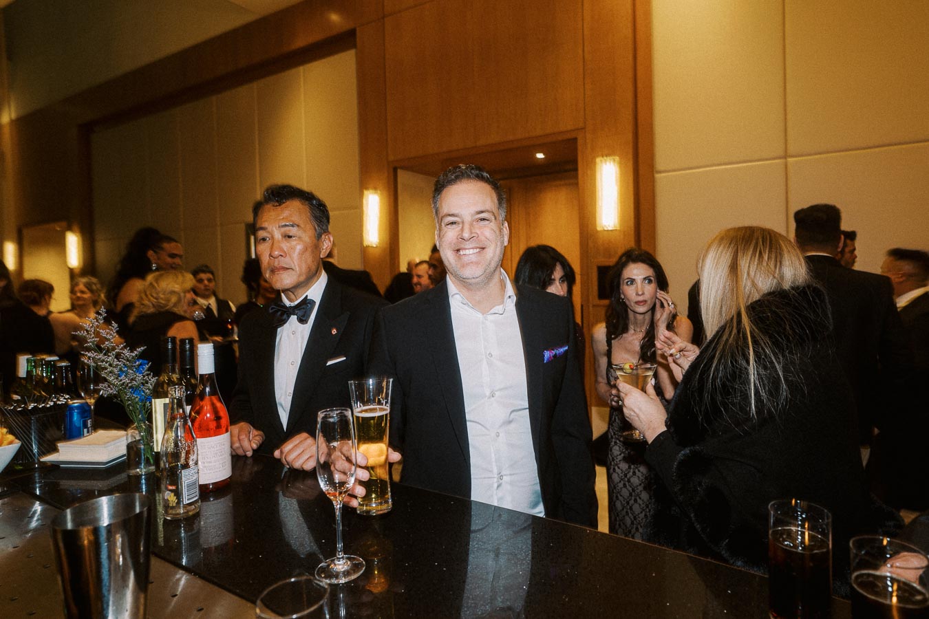 Elegant social gathering with guests in formal attire enjoying drinks at a sophisticated cocktail bar.