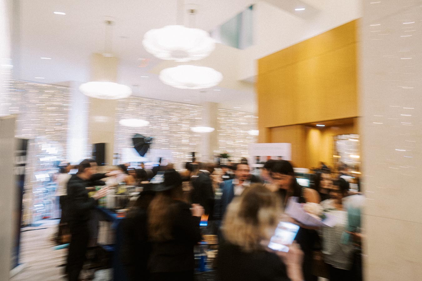 Blurred image of a busy networking event in a modern setting with people interacting, ambient lighting, and elegant decor.