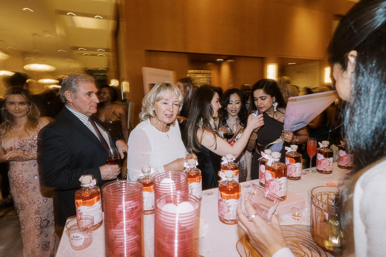 Guests enjoying a lively party scene, sampling beverages at a beautifully arranged table with decorative bottles and glassware, set in an elegantly lit venue.