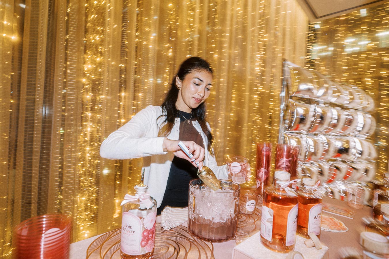 Woman serving drinks at a festive event with sparkling gold decorations in the background.