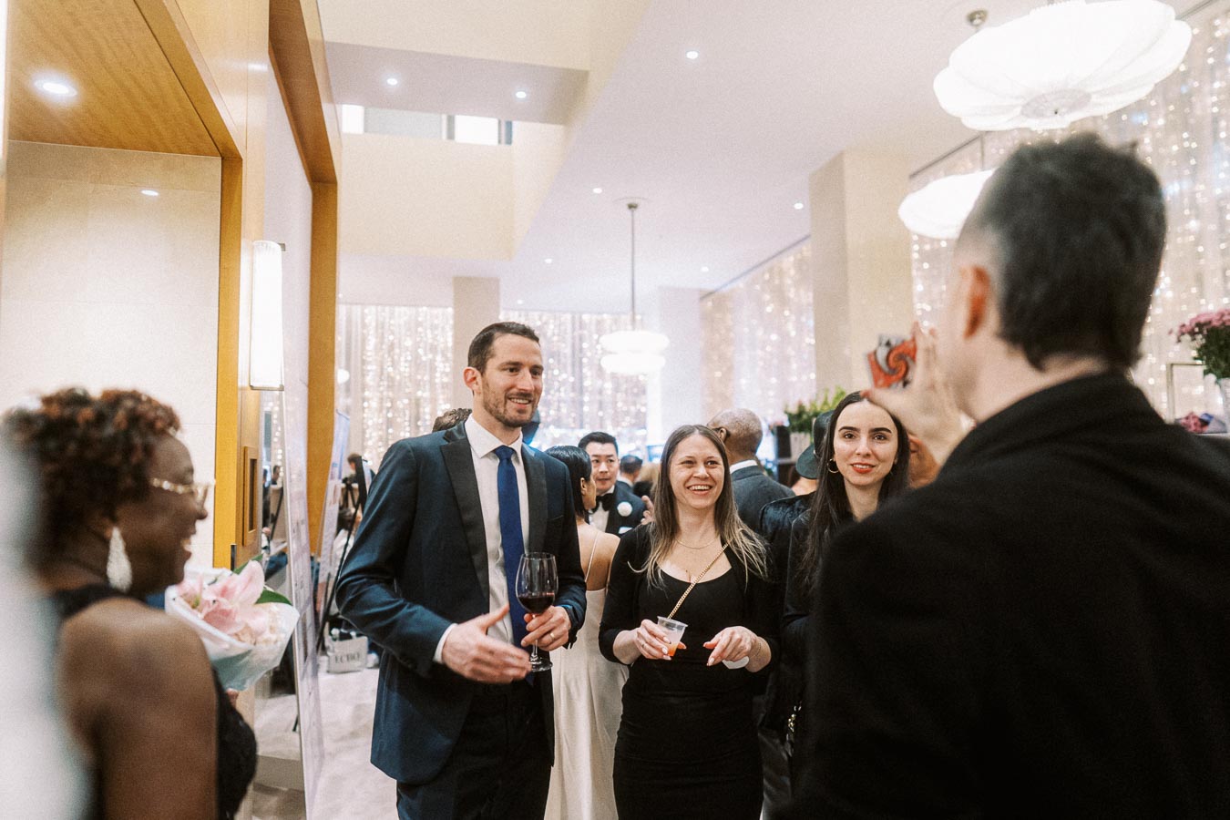 Group of elegantly dressed people enjoying a lively conversation at a sophisticated indoor event with stylish decor and ambient lighting.