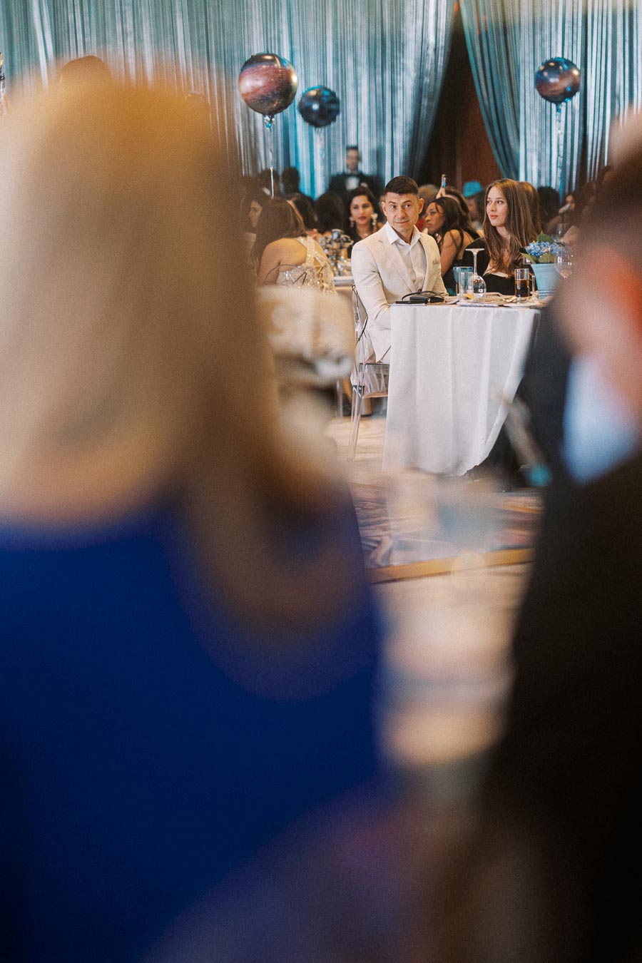 Guests seated at a decorated banquet table during an elegant event, featuring a backdrop of shimmering curtains and planet-themed balloons.