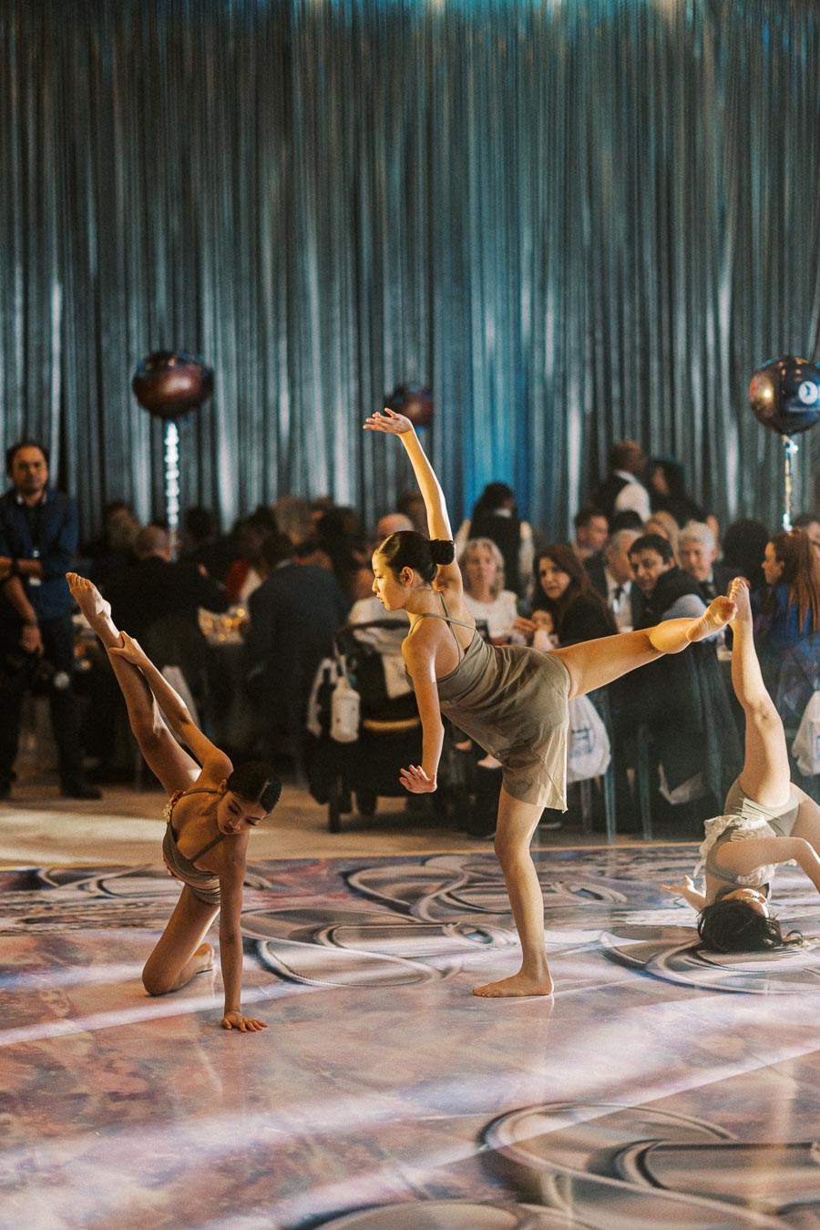 Elegant dancers performing a contemporary routine on a stylish patterned floor at a formal event, with an audience watching in the background.