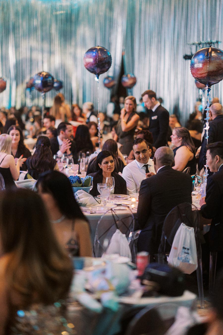 Formal event with elegantly dressed guests seated at round tables, featuring galaxy-themed balloons and ambient lighting, creating a sophisticated atmosphere.