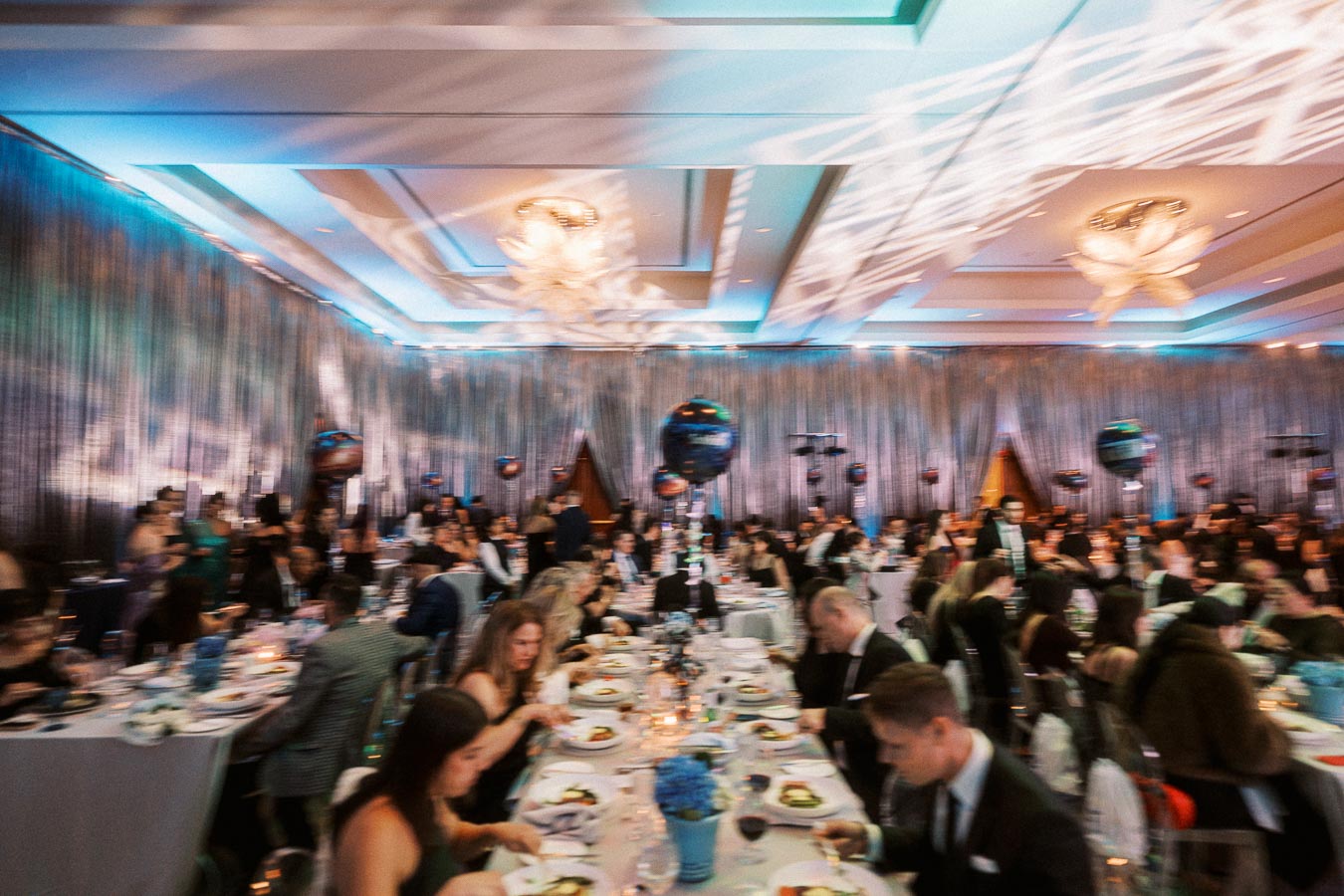 Elegant banquet hall with guests dining at a formal event, featuring elegantly set tables, dim lighting, and decorative balloons.