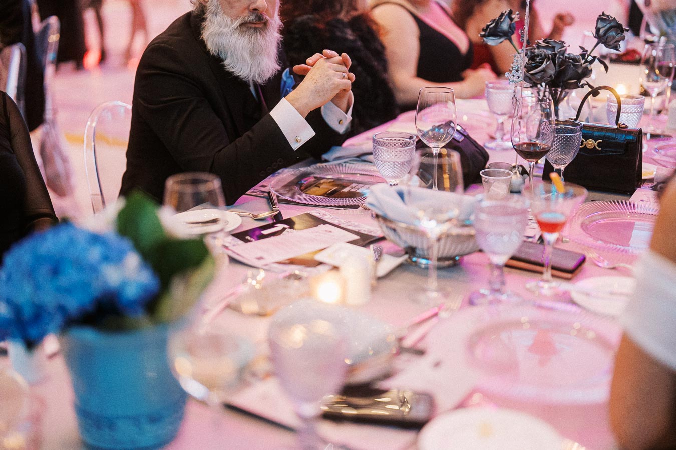 Elegant dinner party setting with guests seated at a beautifully arranged table featuring glassware, floral decorations, and sleek tableware, highlighting a sophisticated and festive ambiance.