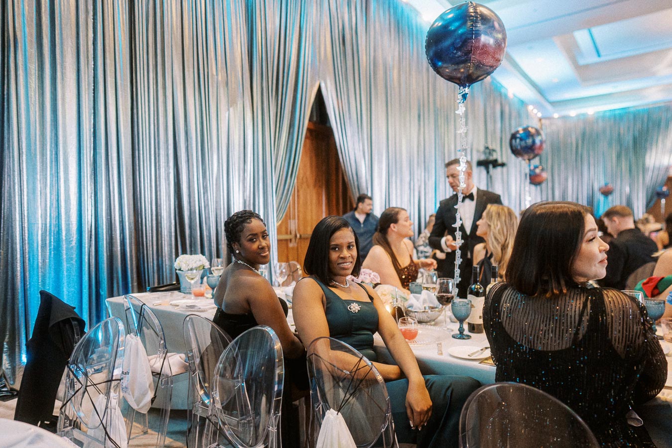 Elegant evening gala with guests seated at a beautifully decorated table adorned with balloons and delicate flower arrangements, creating a sophisticated and festive atmosphere.