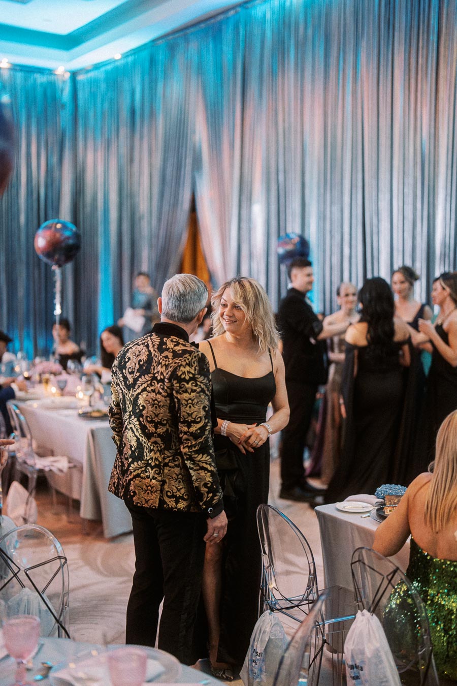 Elegant evening event with guests in formal attire, featuring sophisticated decor, shimmering drapes, and ambient lighting.