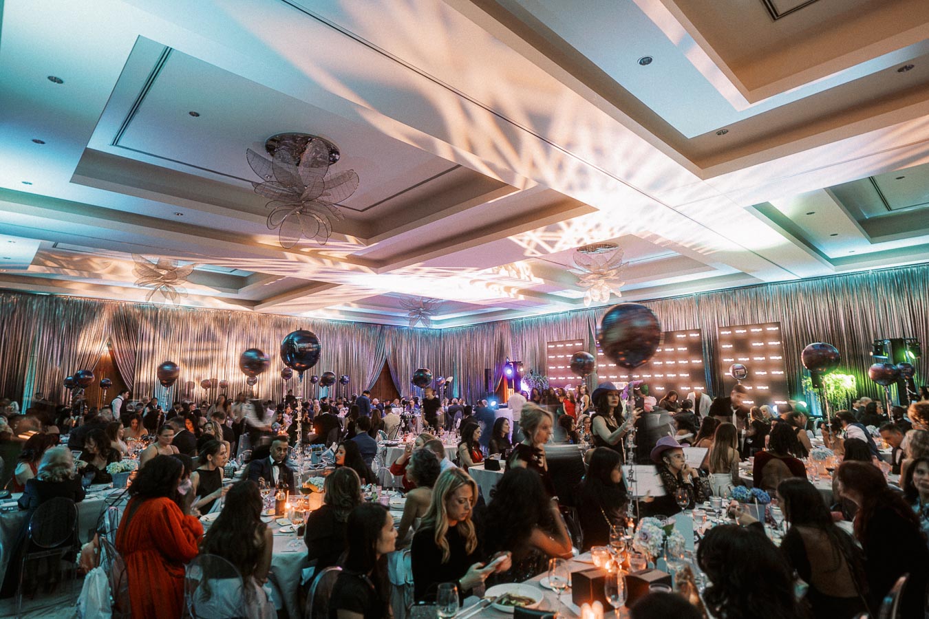 Elegant gala event with guests seated at decorated tables in a luxurious banquet hall, featuring ambient lighting and festive decorations.