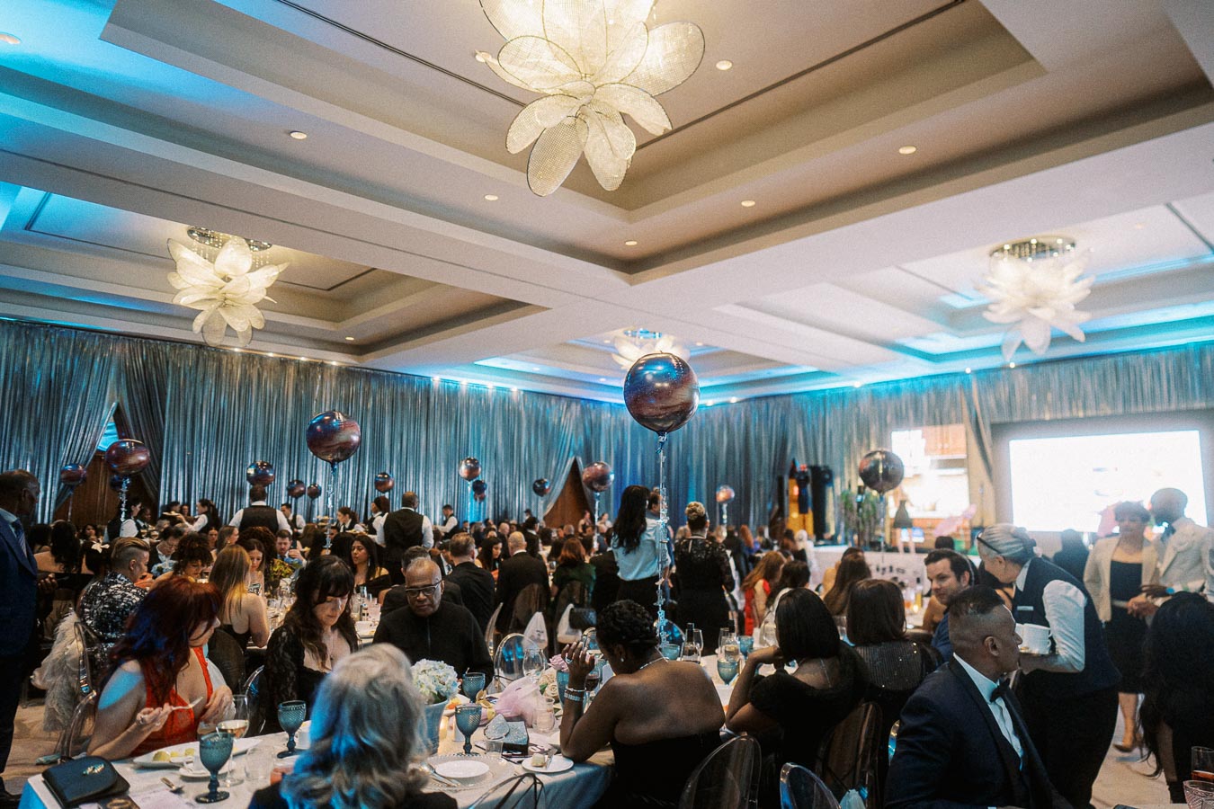 Elegant banquet hall filled with attendees at a formal event, featuring decorative balloons, ambient lighting, and beautifully set tables.